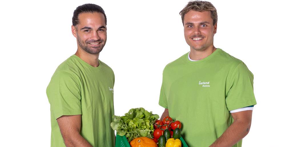 Zwei junge Männer mit Isarlandshirts halten strahlend eine Obst und Gemüsekiste in die Kamera. © Walter Slavik