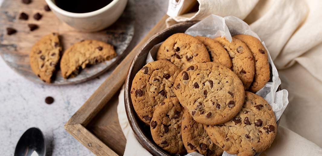 Schoko-Cookies in einer Keramikschüssel, im Hintergrund eine Tasse Kaffee.