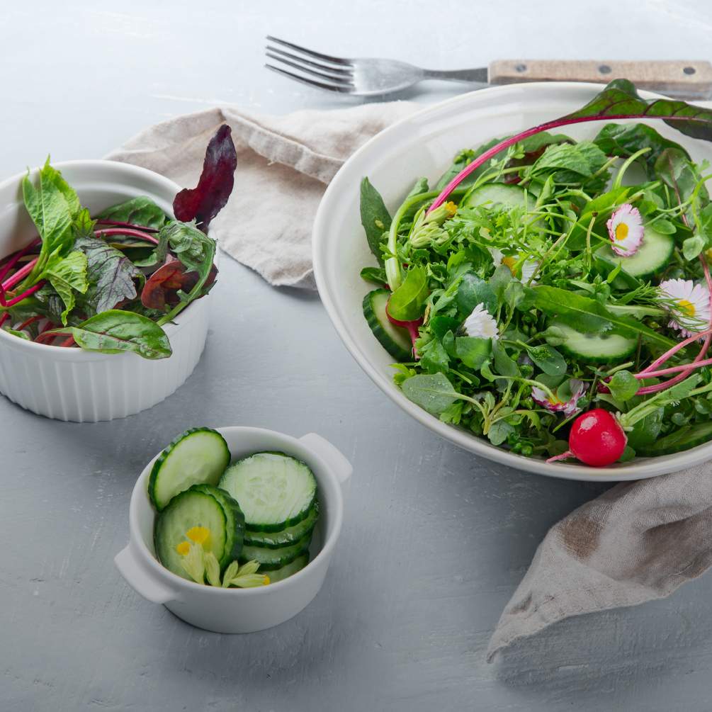 Schüsseln mit buntem, frischem Salat auf weißem Untergrund.