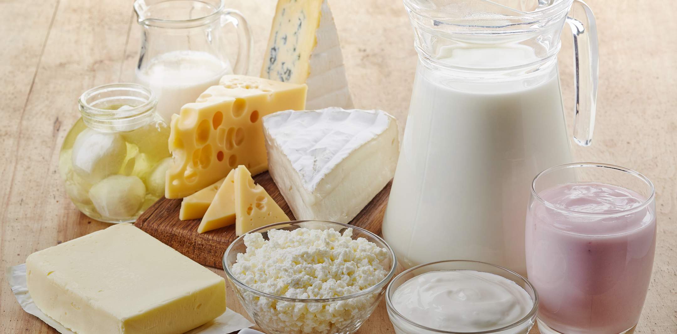 Butter, Joghurt, Emmentaler, Weichkäse, Hüttenkäse und Quark auf einem Holztisch.