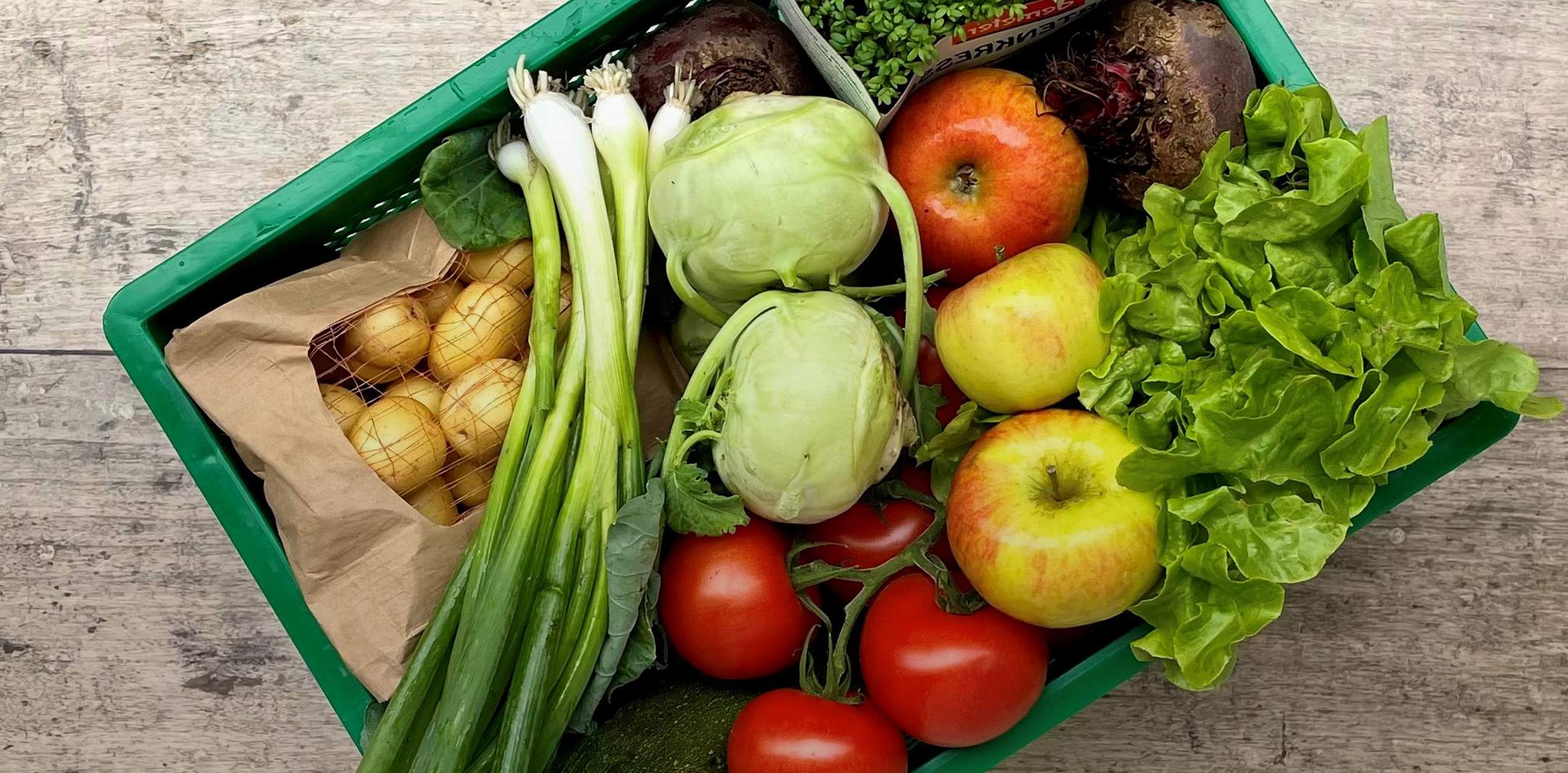 Eine grüne Biokiste gefüllt mit frischem Obst und Gemüse.