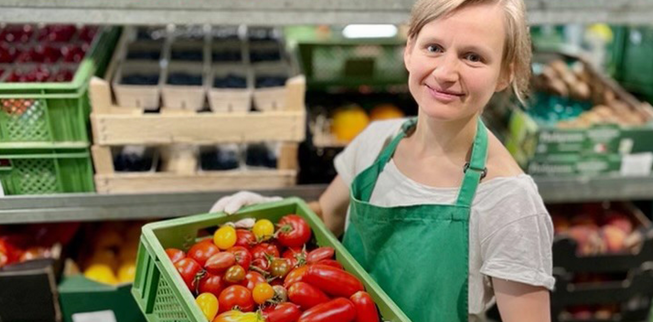 Junge Frau mit einer Kiste voll bunter Tomaten.