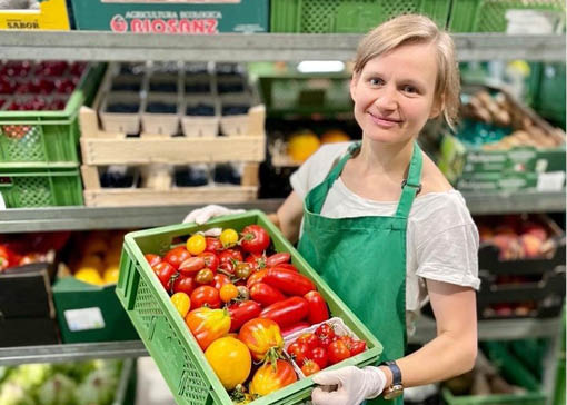 Lächelnde Frau hält eine Gemüsekiste im Obst & Gemüselager.