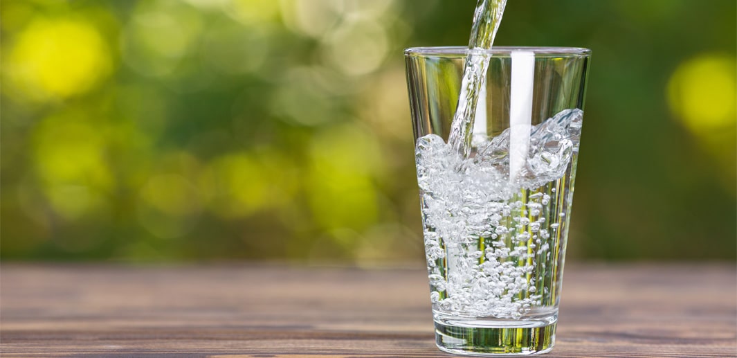 In ein Glas auf einem Holztisch im Freien wird frisches Wasser gegossen.