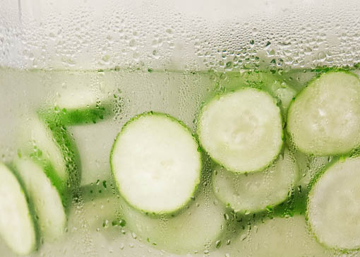 Kälte-beschlagenes Glas, gefüllt mit Wasser und Gurkenscheiben.