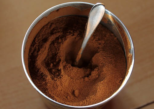 Von obern fotografierte Metalldose mit Kaffeepulver und Löffel auf Holzuntergrund.