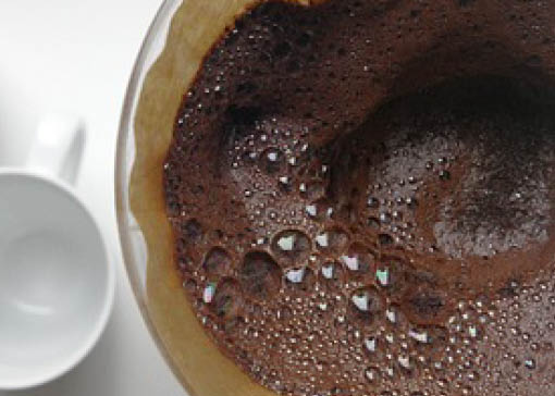 Leere weiße Porzellantasse neben frisch durchgelaufenem Kaffeefilter.