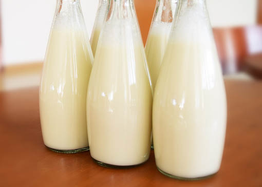 Fünf Milchflaschen auf einer Holztischplatte.
