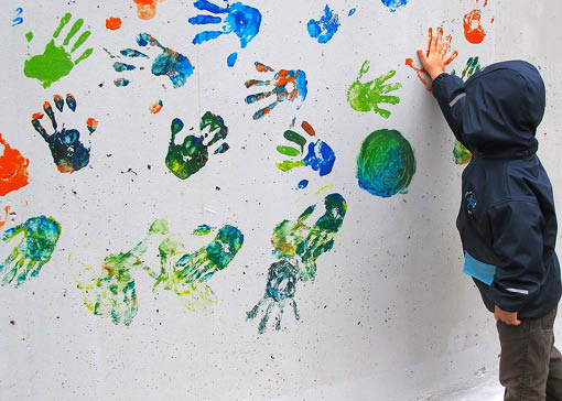 Ein Kind drückt seine Hand an eine mit bunten Handabdrücken verzierte Wand.