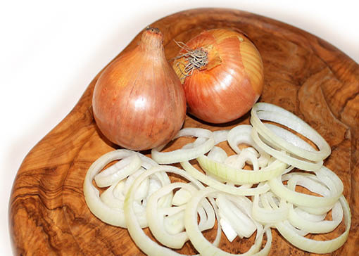 Schön gemasertes Holzbrett mit zwei Zwiebeln und aufgenittenen Zwiebelringen.
