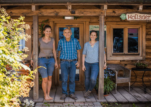 Raphaela und Bernadette Lex mit ihrem Vater stehend auf einer Holzterasse auf ihrem Biohof.