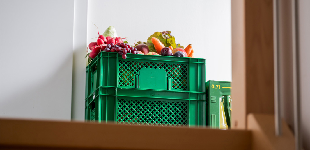 Biokiste mit Obst und Gemüse im Treppenhaus vor einer Wohnungstür