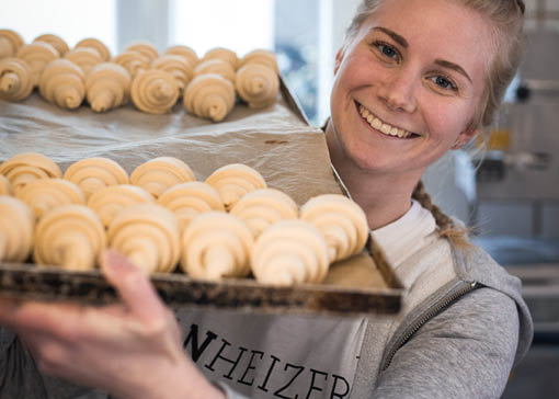 Eine Frau trägt ein Backblech mit Croissants in den Ofen.