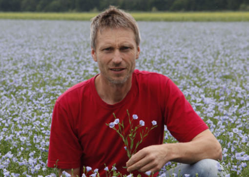 Stefan Jahrstorfer auf einem blühenden Leinenfeld mit einer Leinenpflanze in der Hand.