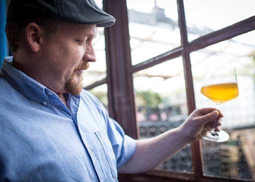 Thomas Girg hält ein Bierglas in der Hand und begutachtet das Bier drin.