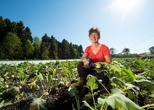 Eine Frau auf einem Feld. Sie hält einen Kohlrabi in der Hand.