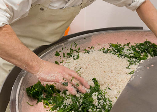 In einem großen Behälter werden die Zutaten für eine Wurst zusammengemischt. Eine Person gibt gerade Gewürze und Kräuter in den Behälter.