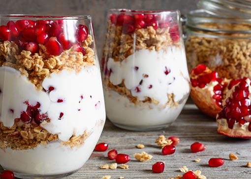Zwei Gläser mit einem Schichtdessert mit Granatapfelkernen, Joghurt und Knuspermüsli