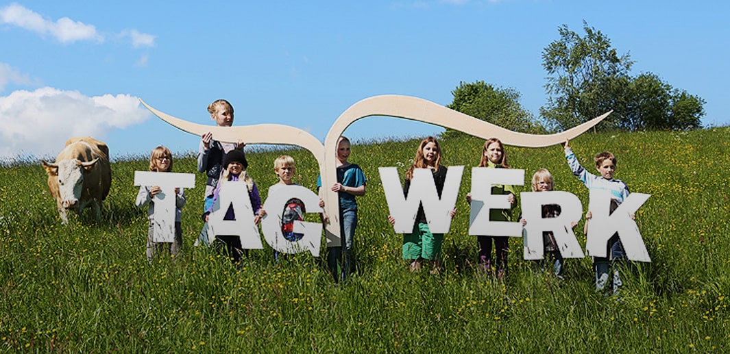 Kinder auf Blumenwiese halten jeweils einen Buchstaben, der den Schriftzug der TAGWERK Genossenschaft bildet.