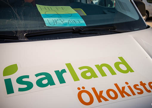 Motorhaube eines Lieferwagens mit Isarland Ökokisten Logo, hinter der Frontscheibe ist ein Plakat mit der Aufschrift Hilfe für die Ukraine.