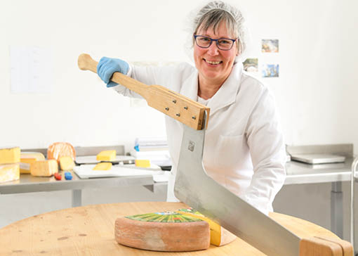 Mitarbeiterin, die im gerade einen großen Laib Käse schneidet.