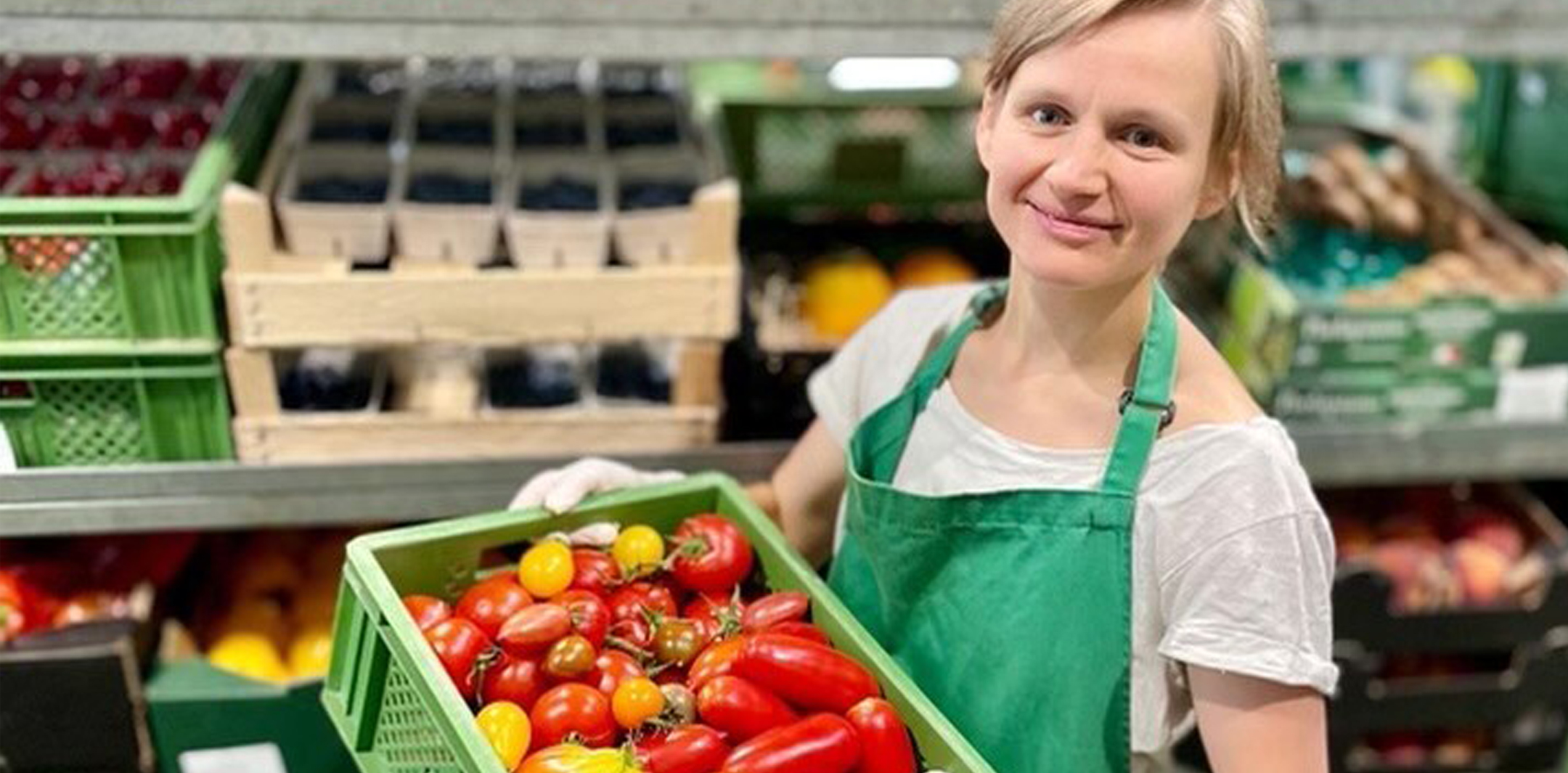 Eine Isarland Mitarbeiterin hält lächelnd eine grüne Kiste mit bunten Tomaten in die Kamera.