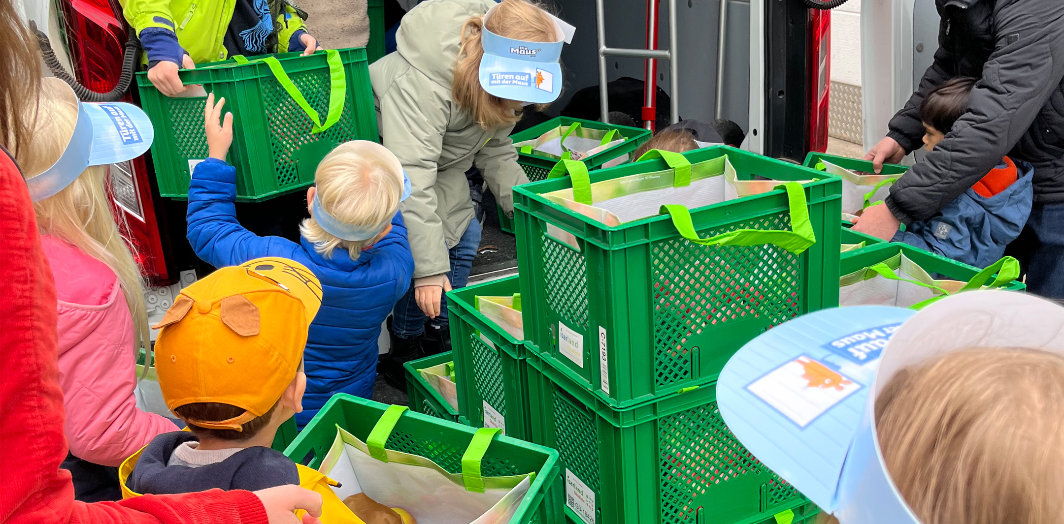 Kinder verräumen beim Maustüröffner Tag grüne Ökokisten.